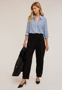Lysblå langærmet bluse med lodrette striber, parret med sorte højhalsede bukser med frontlommer, accessoriseret med en sort læderjakke.