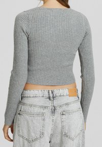 Harmaa ribattu pitkähihaisen crop-top, joka on yhdistetty vaaleansinisempiin farkkuihin, joissa on nahkalamina takana.