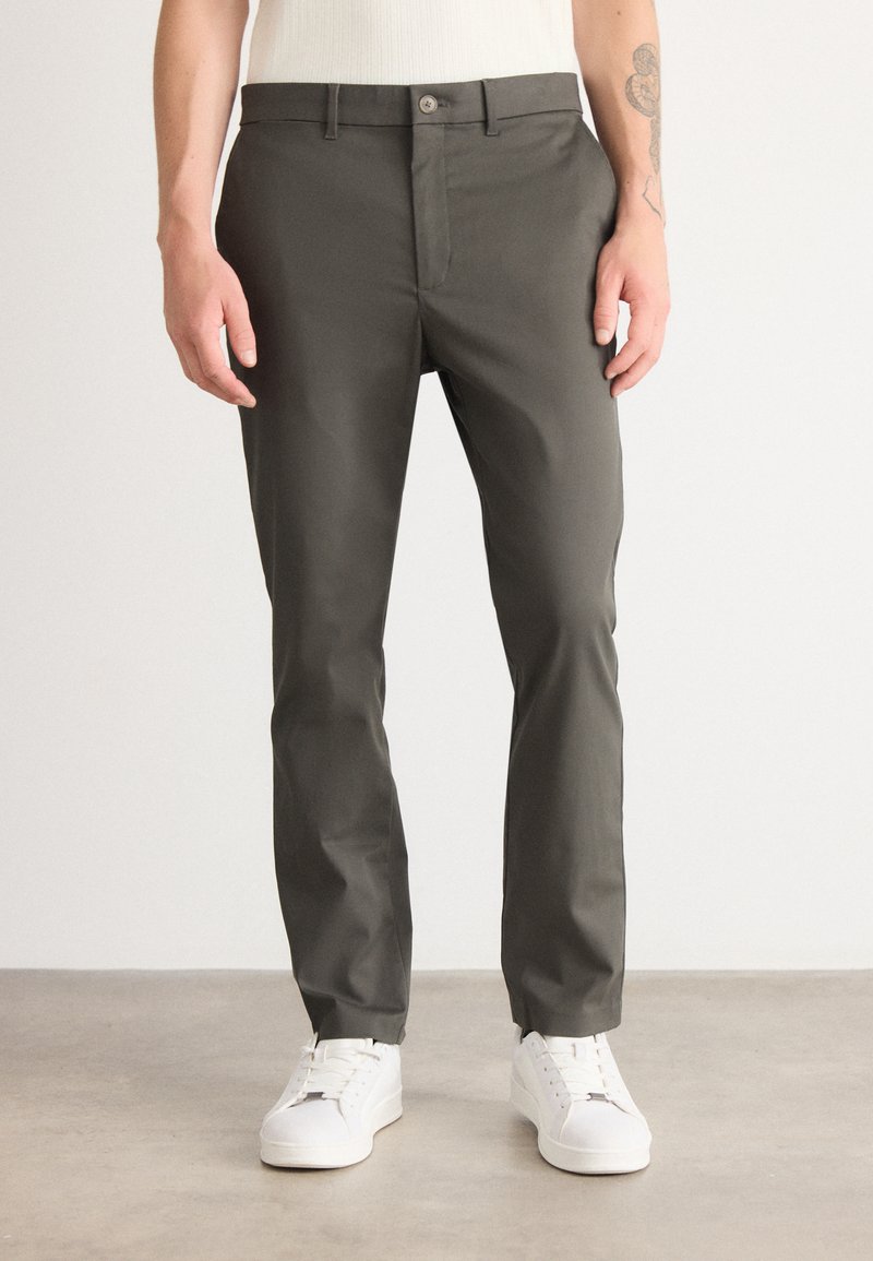 Slim-fit, donkergrijze broek van een zachte stof. Voorzien van een knoopsluiting en zijzakken. Gecombineerd met witte sneakers.