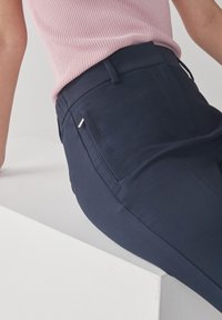Navyblauwe op maat gemaakte broek met een soepele textuur, voorzien van een slim fit, zijzakken en een kleine metalen accent op de achterzak.