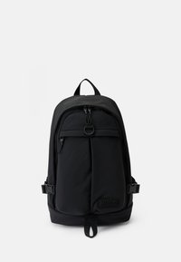 Sac à dos Hugo noir avec une poignée supérieure, une poche zippée à l'avant, des boucles latérales et un logo de marque sur le panneau inférieur avant.