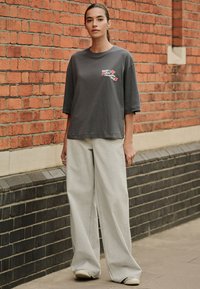 Túlméretezett szürke póló virágmintával, széles szárú világosszürke nadrággal párosítva. Texturált anyag, laza szabás és egyszerű kialakítás.