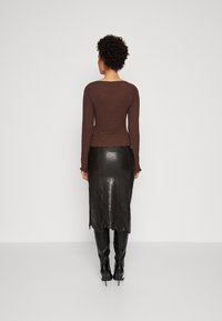 Brun strukturerad långärmad topp i kombination med en svart läderkjol med scalloperad fåll och svarta högklackade knästövlar.