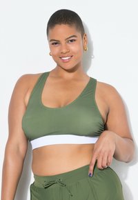 Olivgrön sport-bh med ett vitt elastiskt band; har en racerback-design och slät yta, tillsammans med matchande jogger-shorts.
