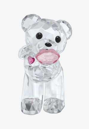 Figurine d'ours en cristal clair avec des yeux noirs, un détail de lèvres roses, et un accent en forme de cœur rose sur sa poitrine. La surface facettée crée une texture brillante.