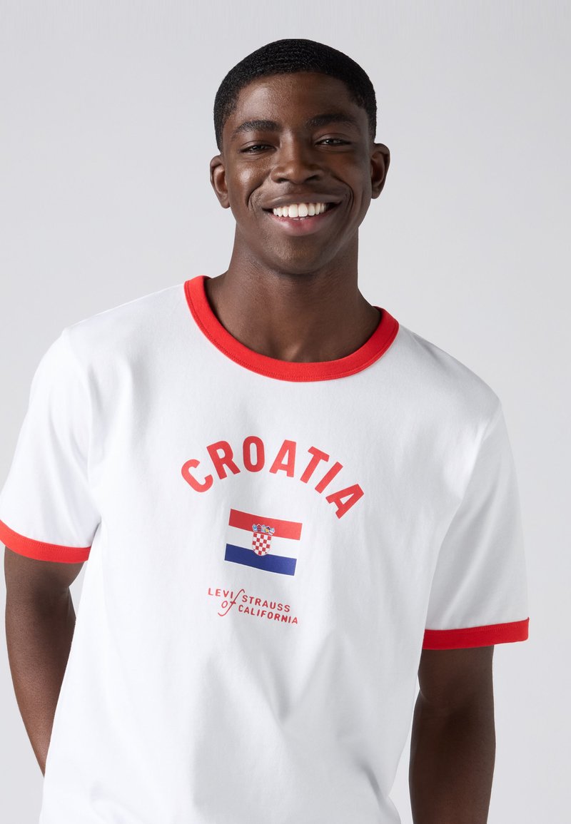 Smiling young man wearing a white T-shirt with red trim featuring the Croatian flag and "Croatia" text on front.