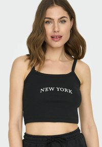 Svart stripete crop top med tynne stropper, med hvit "NEW YORK" tekst over fronten. Enkel design, tett passform, og glatt tekstur.