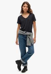 Camiseta negra de cuello en V combinada con jeans azules de talle alto, con los puños enrollados, y botas negras de cordones. Un suéter gris anudado a la cintura.
