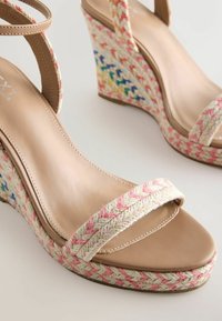 Sandales compensées beige avec brides tressées roses et multicolores, talons, brides à la cheville et semelle intérieure lisse.