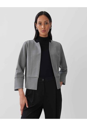 Strukturierte graue Jacke mit geometrischem Muster, offener Vorderseite und Dreiviertelärmeln, kombiniert mit einem schwarzen Top und maßgeschneiderten schwarzen Hosen.