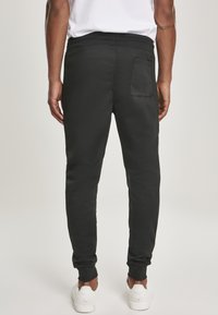 Schwarze Jogginghose mit schmaler Passform, ausgestattet mit einer Gesäßtasche und gerippten Knöcheln, aus einem weichen Baumwoll-Elasthan-Material gefertigt. Kombiniert mit weißen Schuhen.