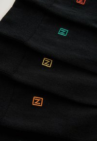 Sorte sokker med farvede "Z" logoer i grøn, orange og gul syet på stropperne. Materialet ser glat ud med ribbede strukturer.