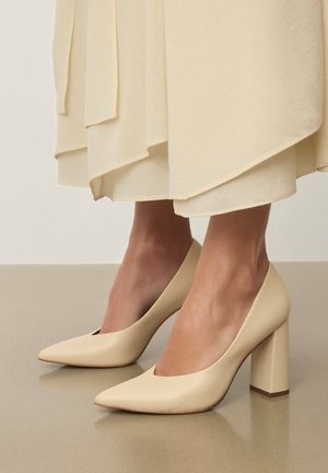 Beežist plokksaabikontsapiga king, millel on terav nina ja avatud küljed. Sile nahk, matt viimistlus, neutraalse taustaga.