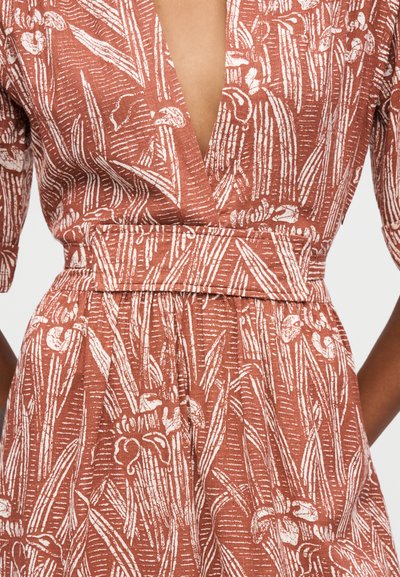 Vestido color óxido con estampado botánico blanco, escote en V profundo, cintura ceñida con cinturón y mangas hasta el codo en una persona.