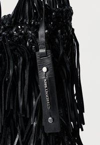 Bolsa de couro trançado preto com textura de franjas, apresentando uma alça de couro preta e uma etiqueta logotipo em relevo prateada.