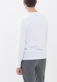 Witte lange mouwen shirt met een ronde hals, zachte textuur en een klein logo op de achterkant; gecombineerd met grijze broeken, gezien vanuit de achterkant.