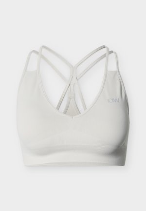 Valge õmblusteta spordirinnahoidja õhukeste risti üle käivate rihmade ja soonilise paelaga, esiküljel paremal pool tagasihoidlik ICANIWILL logo.