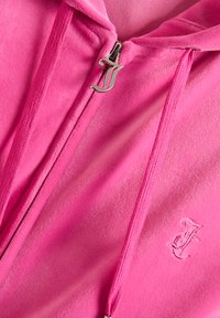 Felpa con zip fucsia con un tirazip argento, caratterizzata da una "J" stilizzata. Texture morbida e dettaglio ricamato con la "J" sul petto.