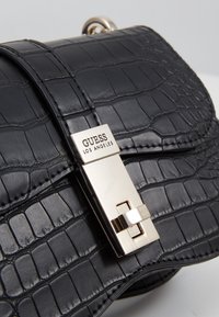 Czarna torebka ze skóry ze wzorem krokodyla, z metalowym zapięciem i tabliczką z marką. Lekko błyszczące wykończenie z wyraźnie zarysowanym kształtem.