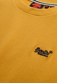 Geel katoenen sweatshirt met een ronde hals, geribbelde halslijn en geborduurd "SuperDry" logo in marineblauw. Zachte textuur, casual ontwerp.