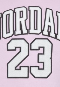 Lys rosa stoff med ordet "JORDAN" i fete svarte og hvite bokstaver over nummeret "23", med detaljer i teksturert søm.