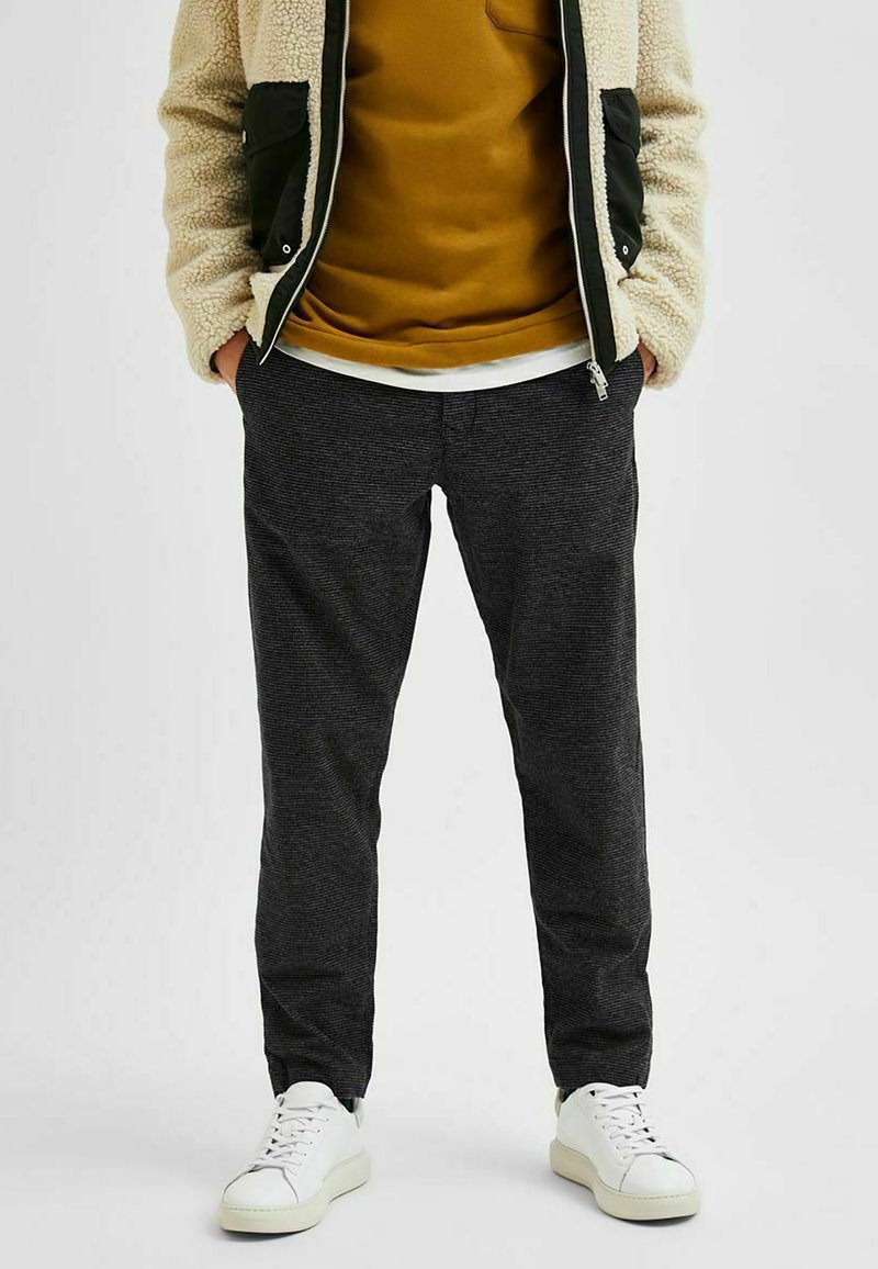 Šedé kalhoty s tenkým střihem a jemnou texturou, kombinované s hořčicovým svetrem a bílými teniskami. Ležérní styl vhodný pro každodenní nošení.