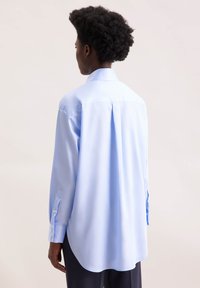 Camicia azzurra chiara a maniche lunghe con colletto classico, taglio dritto e polsini abbottonati, con una pince sul retro per una maggiore libertà di movimento.