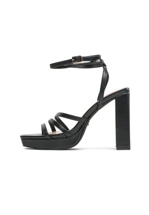 Sandalo nero con tacco alto e plateau, cinturino alla caviglia e più sottili cinturini sopra le dita, mostrato in vista laterale su uno sfondo bianco.