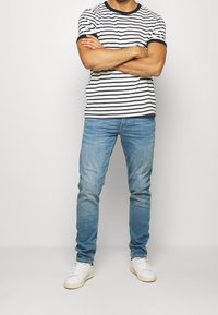 Pruhované tričko s krátkým rukávem v bílé a námořnické modři s kulatým výstřihem, spojené s jemně modrými slim-fit džíny a bílými teniskami.