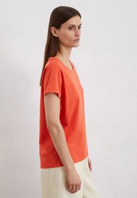 Orange cotton t-shirt with a relaxed fit, short sleeves, and a round neckline. The fabric has a smooth texture and minimal detailing.