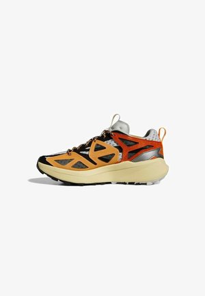 Trail hardloopschoen met beige zool, oranje en zwarte mesh bovenwerk, reflecterende grijze accenten en trekriempjes op de tong en hiel.