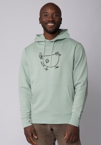 Mintgroene hoodie met een voorzak, voorzien van een zwart lijntekening van een kip en bloemaccenten. Zacht materiaal met een relaxed fit.