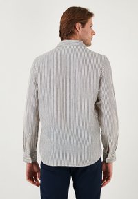 Cămașă cu mâneci lungi în dungi, bej și bleumarin. Include o gulere, manșete cu nasturi și un design drept pe spate cu margine curbată.