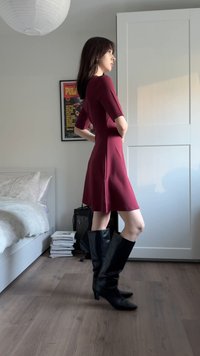 Burgunderrød tettsittende kjole med korte ermer, utsvingt skjørt, kombinert med svarte skinnstøvler til kneet. Glatt stoff og enkelt design.