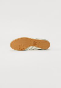 Adidas sneaker talpa világoszöld és krémszínű csíkokkal, textúrált gumi felülettel és barna kör alakú logóval. Lapított design és formázott tapadási minta.