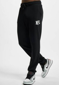 Svarte joggebukser med elastisk livband og snor, med hvit "NFL" logo på låret. Kombinert med grå og hvite joggesko.