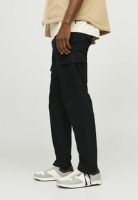 Pantaloni cargo negri cu buzunare laterale, asortați cu adidași albi și gri. Pantalonii au o croială dreaptă și sunt fabricați dintr-un material rezistent.