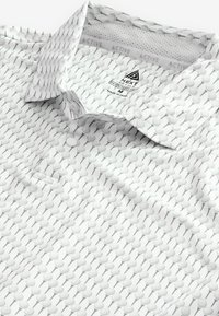 Vit kortärmad polo tröja med ett mönster av grå golftee. Krage med knappslå och luftigt tyg.
