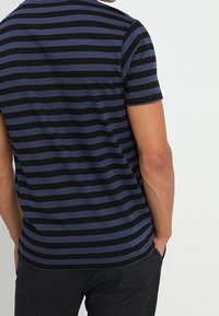 Camiseta de rayas azul marino y negra, de manga corta, corte regular, material de algodón, con textura suave y dobladillo redondeado.