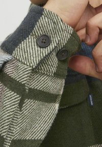Groen en blauw geruite flanellen shirtmanchet met twee zwarte knopen en een zachte, gestructureerde afwerking. Zichtbare stiksels en merklabel.