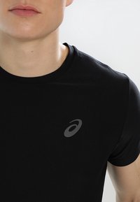 Camiseta atlética negra hecha de una tela texturizada, con cuello redondo y un pequeño logo gris en un lado del pecho.