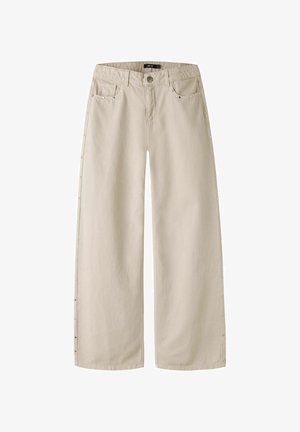 Pantalon beige à jambes larges avec bouton et fermeture éclair à l'avant, passants de ceinture, poches avant et poche monnaie, et petits clous métalliques le long des coutures latérales extérieures.