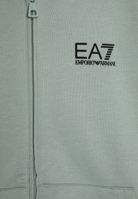 Světle zelená mikina na zip s černým logem EA7 Emporio Armani. Textura látky je hladká s jemným povrchem; obsahuje přední zip.