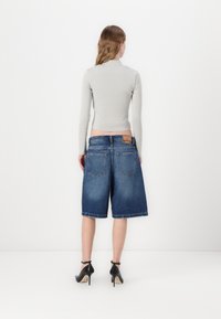 Denim bermuda shorts vaaleansinisessä pesussa suoran lahkeen leikkauksella, joissa on takataskut ja vyötärönauhassa etiketti, yhdistettynä harmaaseen toppiin.
