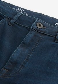 Jeans din denim bleu închis cu croială dreaptă, având un nasture metalic, bucle pentru brâu și cusături deschise pe seamă.