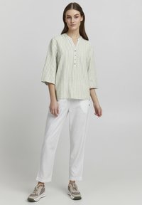 Camisa de rayas verde claro y blanca con escote en V y mangas tres cuartos, combinada con pantalones blancos y zapatillas beige.