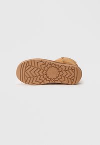 Sandal de tom castanho com uma sola de borracha texturizada, apresentando um padrão geométrico. A parte superior é levemente texturizada, proporcionando um design simples e discreto.