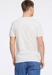 Kermanvärinen puuvillateepaita, jossa on pyöreä kaula-aukko, lyhyet hihat ja rento istuvuus, yhdistettynä sinisiin farkkuihin ja esittelee yksinkertaista muotoilua.