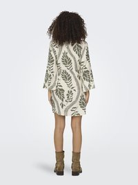 Vestido de manga corta con un patrón de hojas verdes sobre un fondo beige claro, con un ajuste holgado y un corte hasta la rodilla. Incluye botas de tobillo marrones.