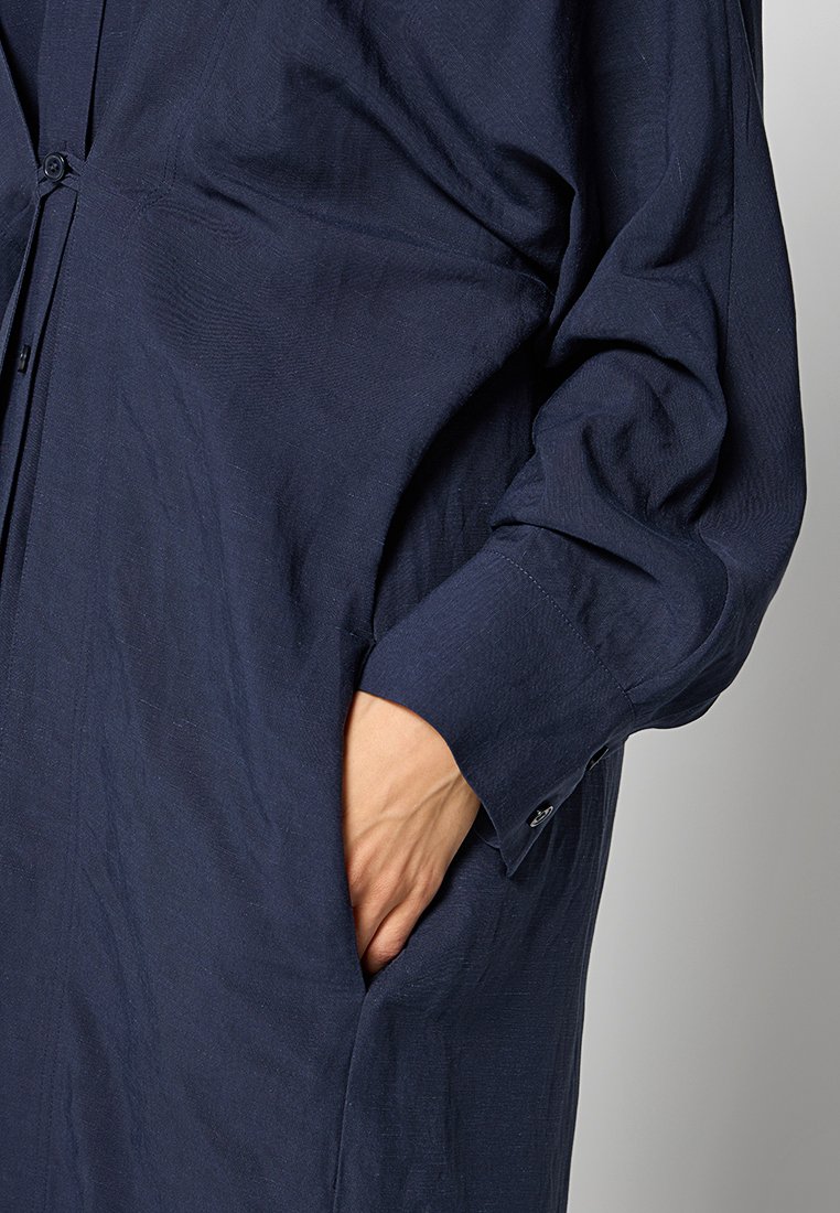 Camicia blu navy con bottoni, maniche lunghe e tasca, realizzata in tessuto leggero e con texture, caratterizzata da una vestibilità comoda e dettagli di cucitura a vista.